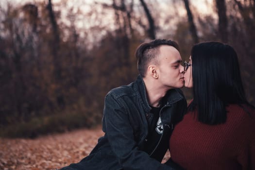 young man and young woman are sitting on a plaid in an autumn forest.