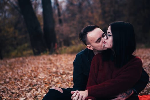 young man and young woman are sitting on a plaid in an autumn forest.