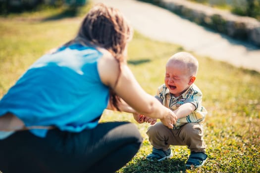 mother and crying toddler son on nature background.