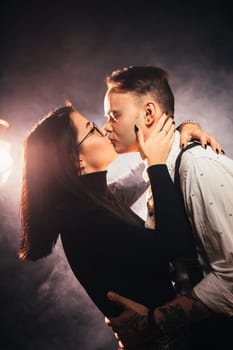 Couple in fashionable clothes on a dark smoky background.
