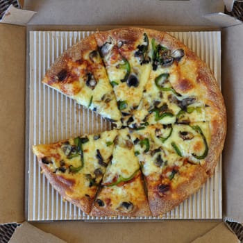 Takeaway pizza with mushrooms and green pepper in cardboard box. Italian fast food background.