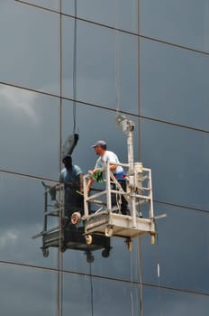 ATHENS, GREECE - JULY 24, 2014: Man cleaning the windows of high rise building glass facade. Working at height dangerous occupation.