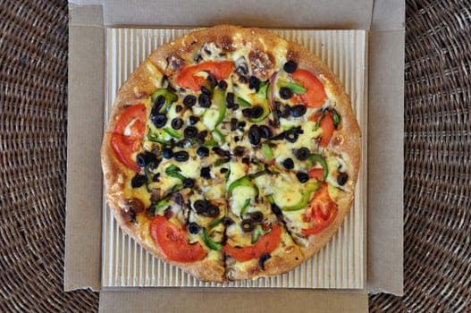 Vegetarian pizza with tomato, olives, pepper, mushrooms and onions packaged in cardboard box. Italian takeaway food background.