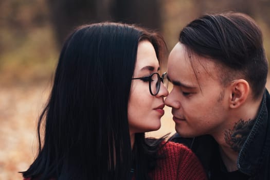 young man and young woman are sitting on a plaid in an autumn forest.