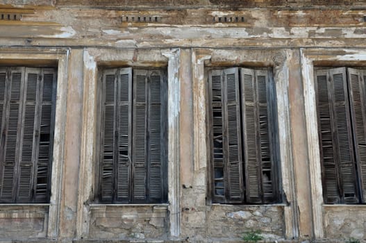 Broken wooden window shutters and chipped wall of a decayed building.