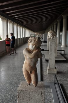 ATHENS, GREECE - SEPTEMBER 2, 2014: Statue of Eros cupid god of love and people visiting stoa of attalos in the ancient agora.