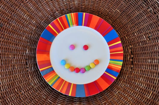Plate with smiling face made from colorful candy. Abstract food background.