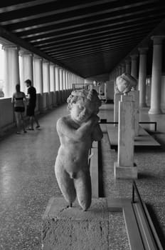 ATHENS, GREECE - SEPTEMBER 2, 2014: Statue of Eros the greek god of love and people visiting stoa of attalos in the ancient agora.