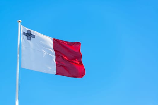 Maltese flag flying in Valletta, Malta against a blue sky
