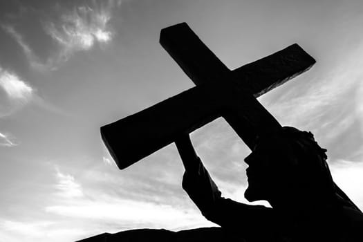 Bronze statue of Jesus carrying his cross, on the way to his crucifixion. Ideal for the easter concept, resurrection and other. Sky with clouds on background.