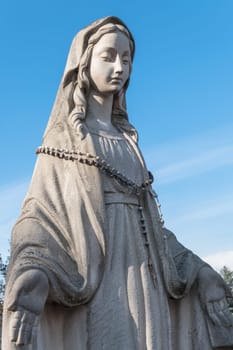 Statue of the Virgin Mary with rosary against the blue sky.