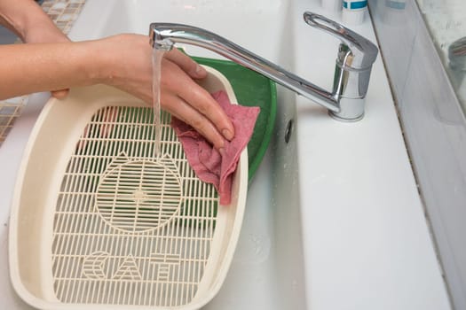 The girl washes the side of the cat tray grate in the sink