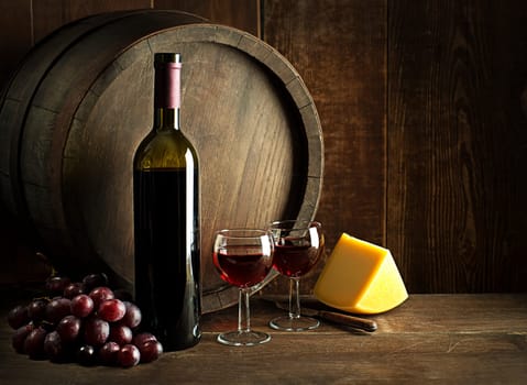 Bottle of red wine with glasses and cheese on wooden and barrel background.