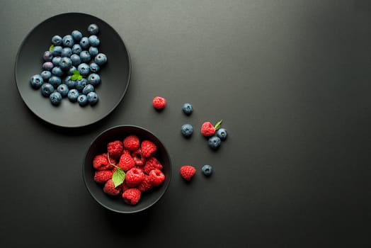 Fresh blueberries and raspberries in a bowl on black background