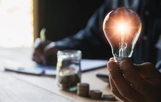 Hand of male holding a light bulb with stack of coins for accounting and creative concept.