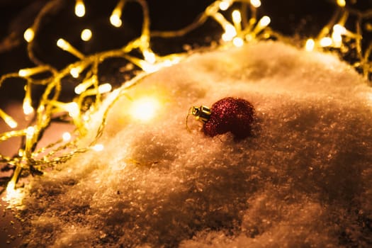 red Christmas ball and luminous garland on the snow.