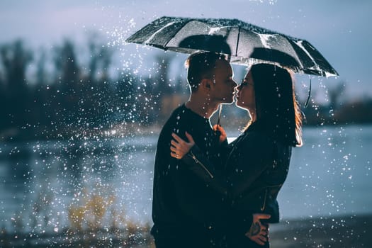 young couple standing under a dark umbrella.