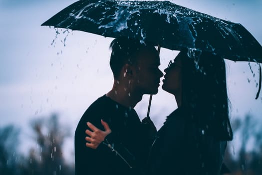young couple standing under a dark umbrella.