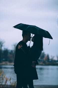 young couple standing under a dark umbrella.