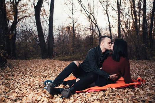 young man and young woman are sitting on a plaid in an autumn forest.
