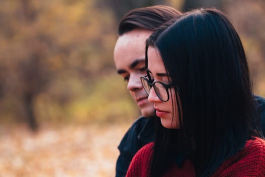 young man and young woman are sitting on a plaid in an autumn forest.