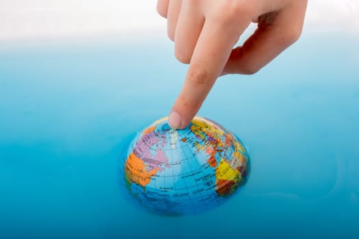 Little globe  with finger on top floating in blue water