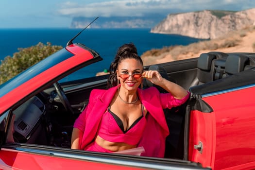 A woman in a pink suit is sitting in a red convertible. She is wearing sunglasses and a necklace