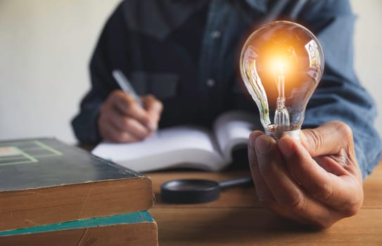 Hand of male holding a light bulb with pile of books for education and creative concept.