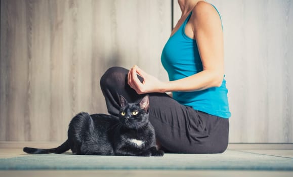 woman doing yoga at home - black cat sitting next to her