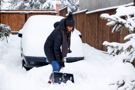 woman with shovel cleaning snow aeound car. Winter shoveling. Removing snow after blizzard