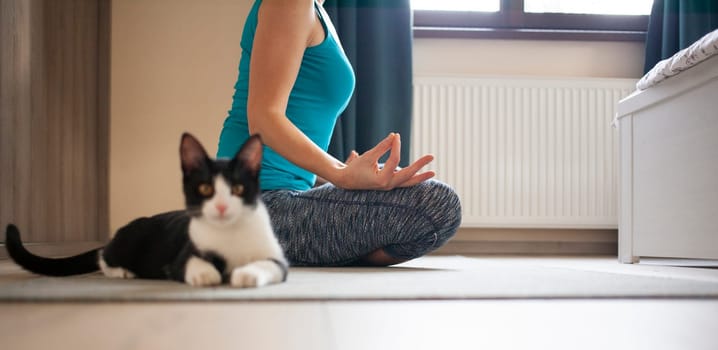 woman doing yoga at home - black cat sitting next to her