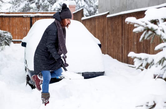 woman with shovel cleaning snow aeound car. Winter shoveling. Removing snow after blizzard