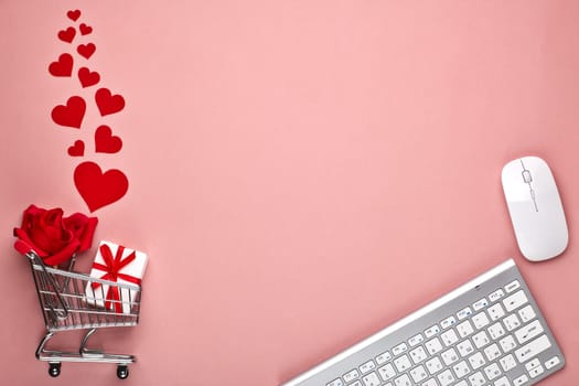 Shopping trolley, Computer keyboard and mouse, gift box, flower and decorative red hearts on pink background with copy space. Concept of internet shopping. Valentine's day, Mother's day, wedding