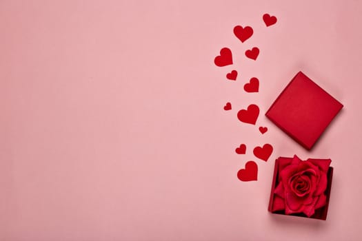 Red decorative hearts and gift box with rose on a pink background with copy space. Top view. Valentine's Day card. Design element for romantic greeting card, wedding invitation