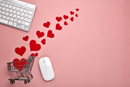 Shopping trolley, Computer keyboard and mouse, decorative red hearts on pink background with copy space. Concept of internet shopping. Valentine's day, Mother's day, wedding
