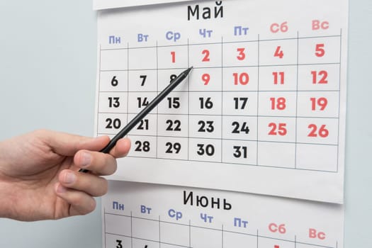 Pencil hand indicates long weekends and holidays on a wall calendar