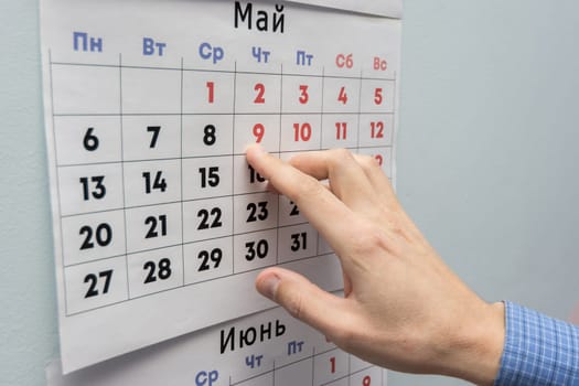 Office worker's hand indicates May holidays on a wall calendar sheet