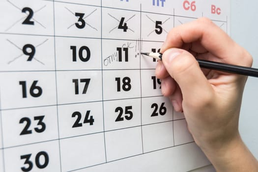 The hand with a pencil writes the word vacation in the wall calendar