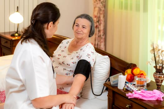 Female doctor checking blood pressure to senior woman at home. Elderly healthcare concept.