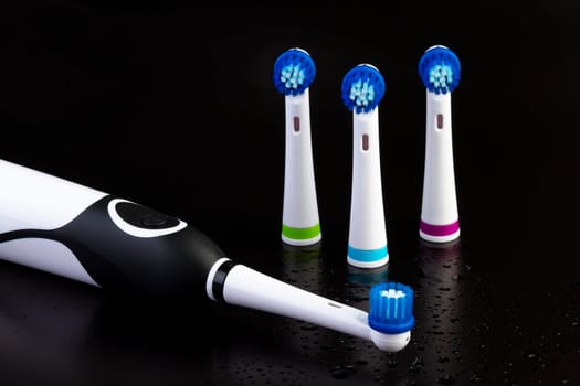 Electric rechargeable toothbrush with three toothbrush heads on black background with water drops. Focus on the power button.