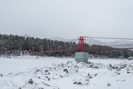 Suspension hanging bridge above winter frozen mountain Katun river, Altai mountains, Siberia, Russia