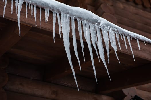 Closeup photo of the Icicles hang from the roof of wooden house