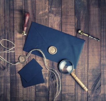 Blank black retro stationery on wood table background. Envelope, wax seal, stamp, magnifier and spoon. Flat lay.