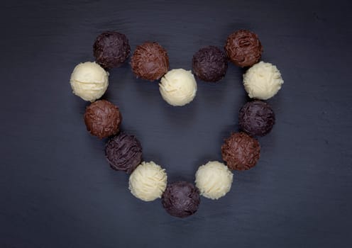 Chocolate truffles assortment heart shape on black stone.