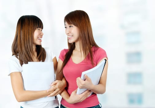 Two happy Asian students with books talking in school campus.