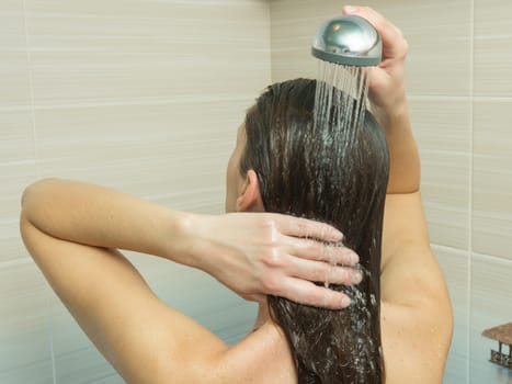 The girl washes her hair in the bathroom under the shower