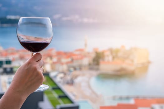 Woman holding glass with red wine on the balcony of her apartment in the Budva town, Montenegro