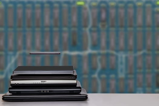 Stack of laptop computers and a smartphone. A pile of computers and a smartphone on a bright table against bright blurred blue digital electronic circuit board texture background. PCB. Template for your product display montage.