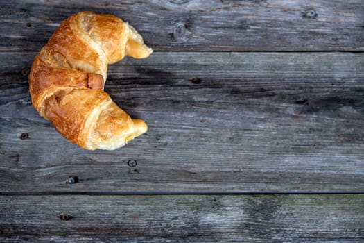 one fresh french croissants on wooden ground