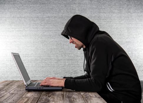 hacker in black hoody with laptop  in front of  gray background
